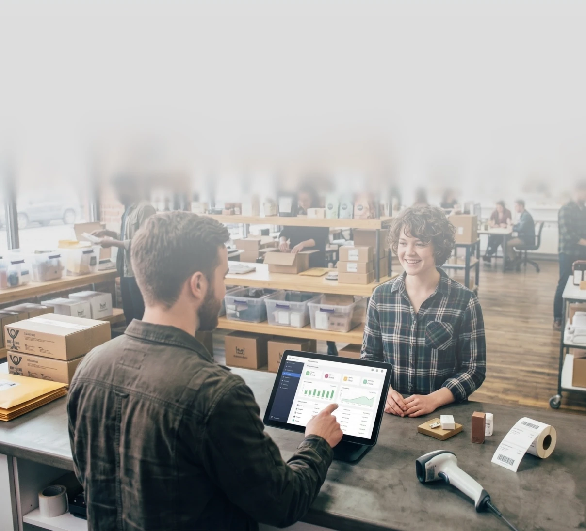 Two people behind a shipping counter checking a support dashboard on a tablet.